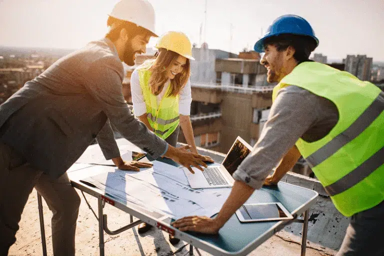 A group of construction professionals reviews plans on a rooftop, collaborating around a laptop — How to Be a Better Construction Project Manager article cover