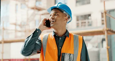 10 Unmistakable Signs Your Construction Team Needs to Invest in Construction Software 1 A construction worker in safety gear talks on the phone at a jobsite — 10 Unmistakable Signs Your Construction Team Needs to Invest in Construction Software article