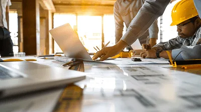 Construction team gathered around a table reviewing blueprints and documents, with a laptop and hard hat visible — 9 Best Practices for Construction Change Orders article