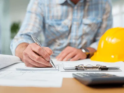 A Step-By-Step Guide on How to Write a Construction Change Order 2 A close-up of a contractor filling out paperwork at a desk, with a hard hat, documents, and calculator nearby — A step-by-step guide on how to write a construction change order article