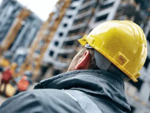 A construction worker in a yellow hard hat observes an active building site — Construction Budget Categories article
