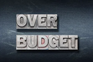 The words “OVER BUDGET” displayed in bold metal letterpress type — Why Do Construction Projects Go Over Budget article