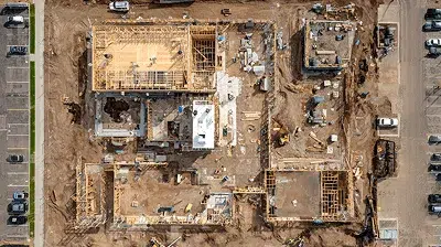 A top-down aerial view of an active construction site, showing building foundations, framing progress, equipment, and crews working across multiple zones — 7 Most Common Construction Billing Methods article