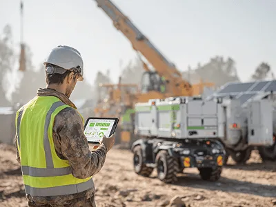 7 Tips for Avoiding Common Contractor Invoicing Mistakes In Construction 1 A construction worker uses a tablet to monitor project data on an active job site, with heavy machinery in the background under clear daylight — 7 Tips for Avoiding Common Contractor Invoicing Mistakes In Construction article
