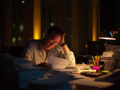 A man works late at night under a desk lamp, reviewing reports and documents — The Role of Construction Quantity Surveyors article