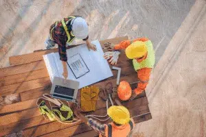 An overhead view of a construction team reviewing project plans and digital charts on-site — How To Improve Change Order Management in 2025 article cover
