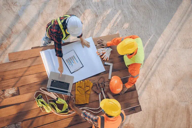 Blog 11 An overhead view of a construction team reviewing project plans and digital charts on-site — How To Improve Change Order Management in 2025 article cover