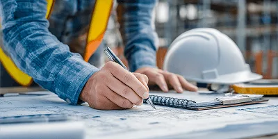 Major Infrastructure Projects: How Long-Lead Procurement and Market Volatility Are Reshaping Construction Cost Management 2 Construction engineer reviewing technical drawings on-site with hard hat and safety vest